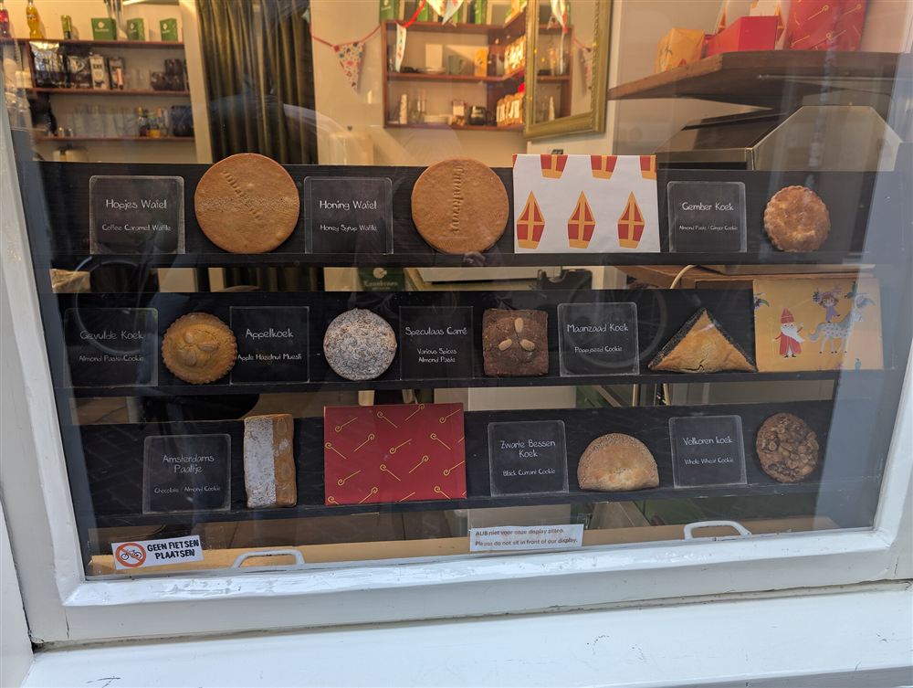 A shop window with neat rows of labelled cakes and biscuits on dark shelves